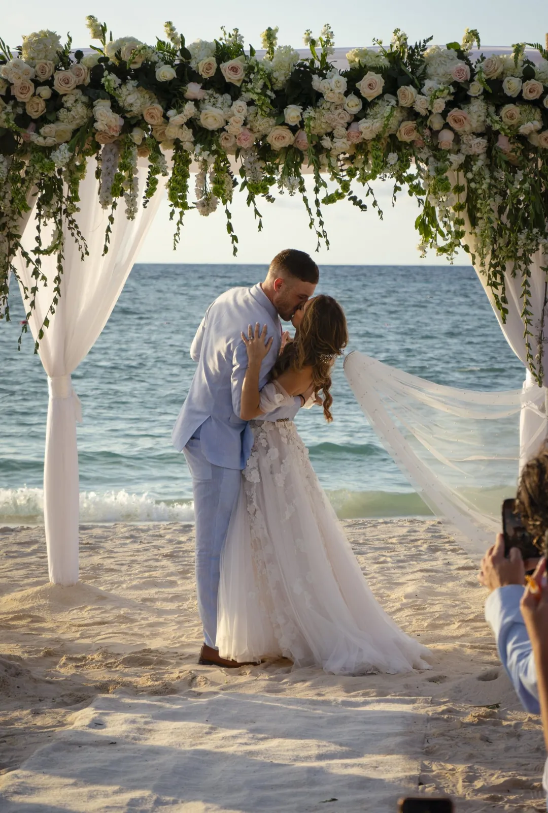 Bride and groom kissing under a flower arch on the beach in Aruba